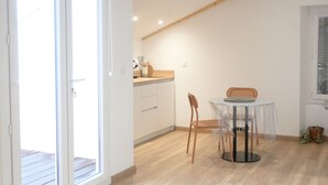 A bright kitchen with wooden beams, a dining table with chairs, and a window with blinds. - Lovely studio with modern comforts and exceptional view (Calvi)