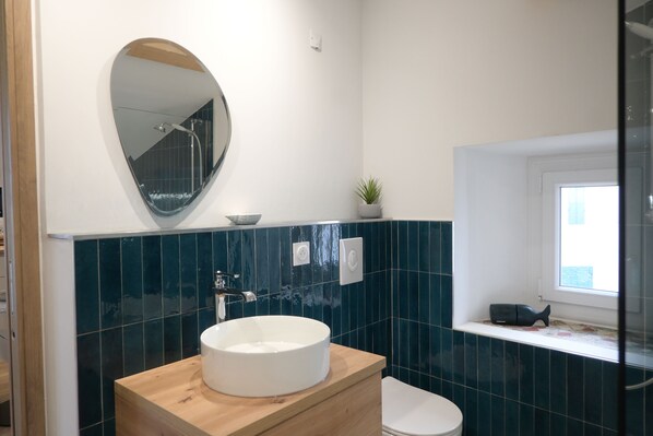 A bathroom with a round white sink, a wooden vanity, a mirror, a potted plant, and a window with a view of the outside. - Lovely studio with modern comforts and exceptional view (Calvi)