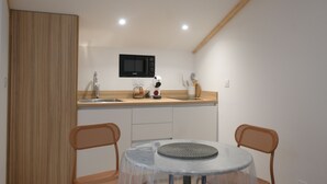 A compact kitchen with a microwave, sink, and wooden cabinets. There is a round table with chairs and a clear glass top. - Lovely studio with modern comforts and exceptional view (Calvi)
