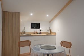 A compact kitchen with a microwave, sink, and wooden cabinets. There is a round table with chairs and a clear glass top. - Lovely studio with modern comforts and exceptional view (Calvi)