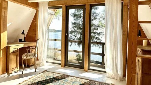 A room with a desk, chair, and large windows overlooking a body of water.