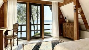 A bedroom with a large window, wooden furniture, and a view of a lake.