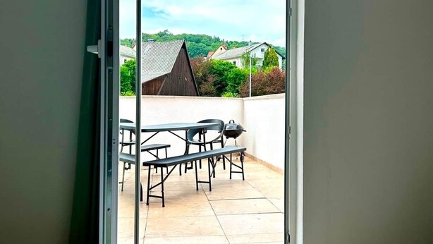 Une chambre à coucher avec un lit et une porte-fenêtre coulissante donnant sur une terrasse extérieure équipée d’une table et de chaises.