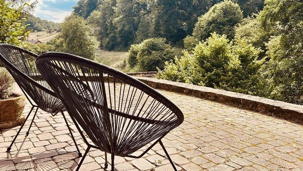 Ein gepflasterter Außenbereich mit zwei schwarzen Metallstühlen und einem Blumentopf.