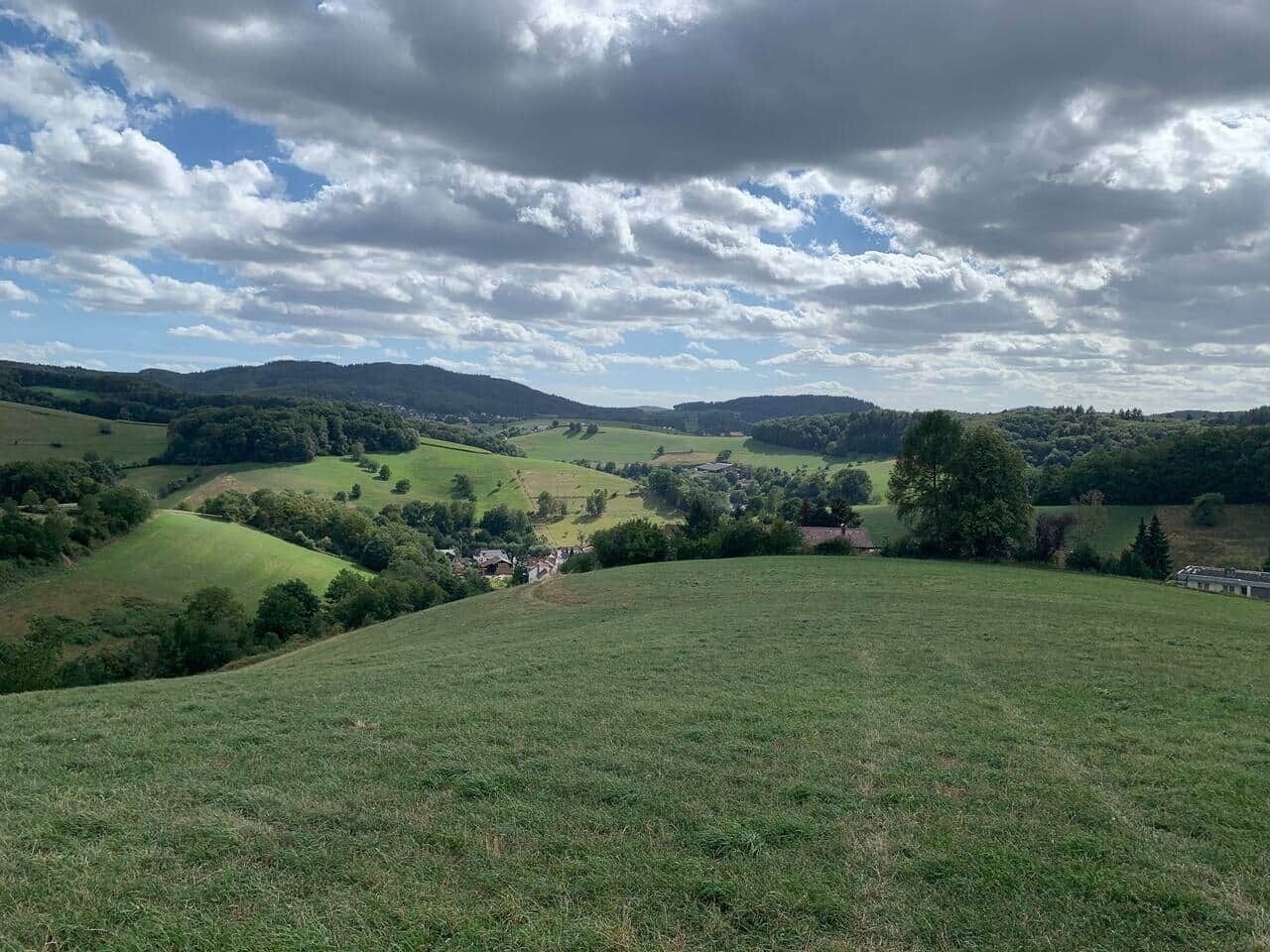 A panoramic view of a rural landscape with rolling hills, scattered trees, and a small village in the distance.