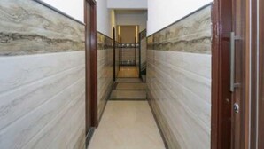 A narrow hallway with marble walls and a wooden door on the right. - Hotel O The Grand Venice Mall (Noida)