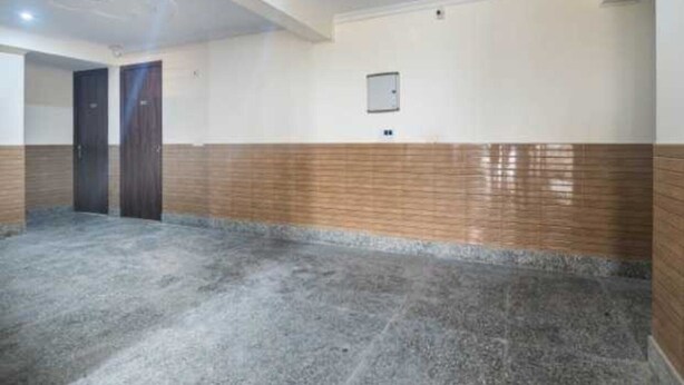 A hallway with a tiled floor, a wooden accent wall, and a ceiling with recessed lighting. - Hotel O The Grand Venice Mall (Noida)