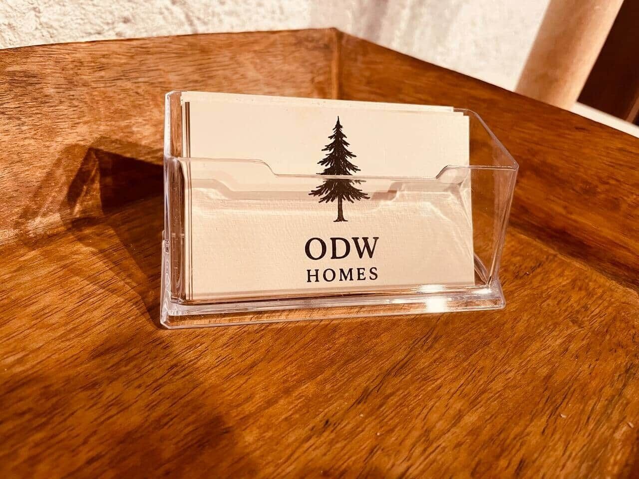 Uma caixa de armazenamento de plástico transparente com a inscrição "ODW HOMES" e um desenho de árvore, colocada sobre uma superfície de madeira.