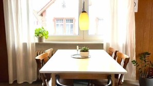 Een eethoek met een tafel, stoelen, een hanglamp en potplanten.