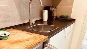 Cocina compacta con un lavamanos integrado, encimera de madera y refrigerador blanco con las puertas abiertas.