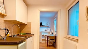 Una cocina estrecha con un lavamanos, un hervidor y una ventana.