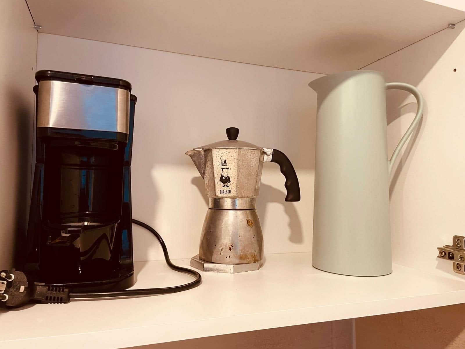A kitchen shelf with a coffee maker, a kettle, and a power cord.