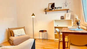 Una habitación acogedora con cama, escritorio con silla, una mesita y estante con objetos decorativos.