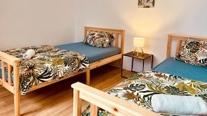 Una habitación con dos camas de madera, cada una con una colcha y almohadas a cuadros con motivos de hojas tropicales. Entre las camas hay una mesita de noche con una lámpara.
