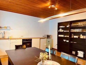 Une cuisine moderne avec un coin repas, dotée d’un plafond en bois, d’un four à micro-ondes encastré et d’une grande bibliothèque noire remplie de verres et de cristaux.