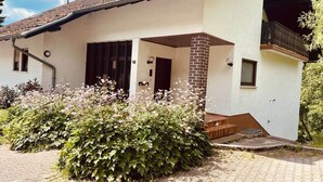 Uma casa de dois andares com telhado de telhas, entrada de tijolo e uma pequena varanda.