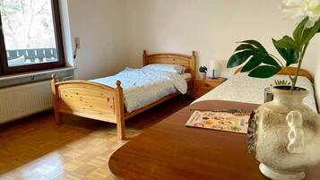 A small bedroom with a wooden bed, a bedside table, a vase with a flower, and a window with a view of trees.