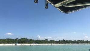 Ein Strand mit klarem türkisblauem Wasser und einer Baumreihe im Hintergrund.
