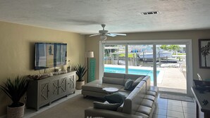 Ein Wohnzimmer mit einem beigen Sofa, einem Fernseher und einem Deckenventilator.