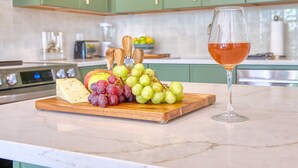 A kitchen counter with a wooden board holding cheese, grapes, and an apple, and a wine glass. - Beautiful Spacious 3BR/3BA Bed-Stuy Brownstone Duplex, King Bed, Heated Floors (Brooklyn)