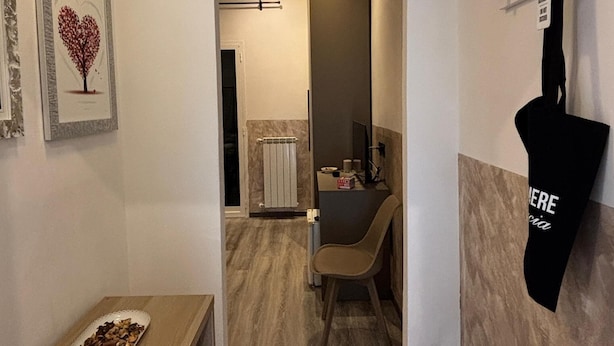 A hallway with a wooden bench, a radiator, a chair, and a black bag hanging on the wall. - Casa lucia (La Spezia)