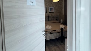 A hotel room with a bed, a nightstand, a lamp, and a door with a nameplate. - Casa lucia (La Spezia)