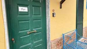 A green door with a nameplate reading "Enza," a mailbox, and a blue metal bench outside a building with yellow and stone walls. - Casa lucia (La Spezia)