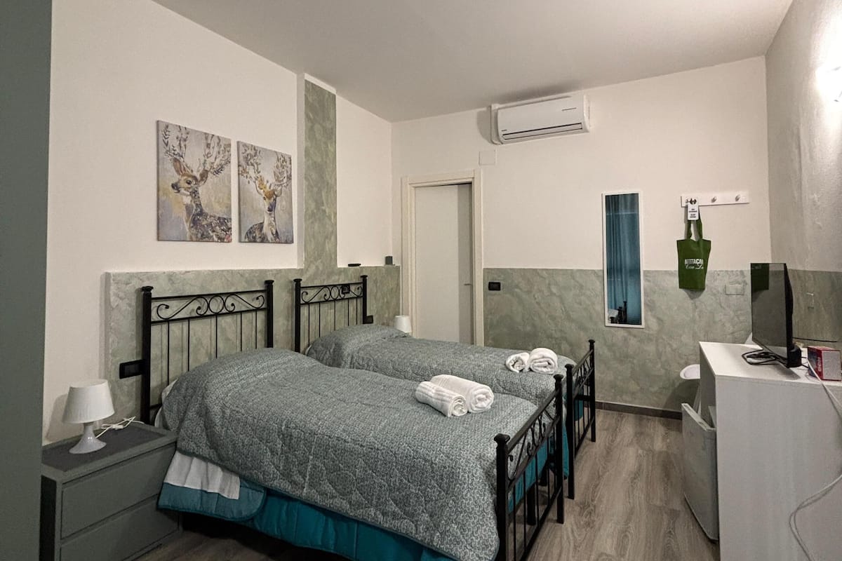 Une chambre avec deux lits, une table de chevet avec une lampe, un miroir, un appareil de climatisation et un petit bureau avec une télévision.