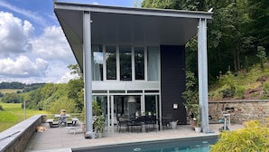Una casa moderna de dos pisos con piscina, mobiliario exterior y un muro de piedra.
