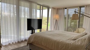 Un dormitorio con una cama grande, una televisión de pantalla plana, una lámpara de escritorio y una silla.