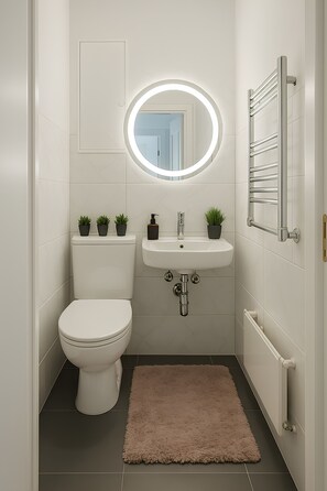 A compact bathroom with a toilet, sink, and mirror. - StadtLicht Apartment with Balcony (Koblenz)