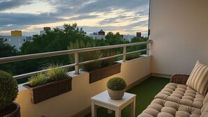 En balkong med en soffa, stolar och blomkrukor, med utsikt över stadsbilden.