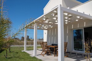 Eine überdachte Terrasse im Freien mit Tisch und Stühlen, einer Pergola und Blick auf das Meer.