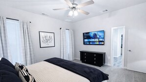 Un dormitorio con cama, ventilador de techo, televisor en la pared y un cuadro enmarcado.
