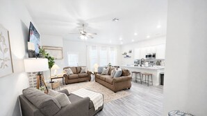 Una sala de estar moderna con dos sofás, una mesa de centro y una zona de cocina con microondas y armarios.