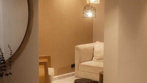 Une salle de bain moderne avec un miroir rond, un canapé beige et une table d’appoint en bois agrémentée d’objets décoratifs.