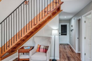 A staircase with wooden steps and black railings, a chair with a plaid pillow, a small wooden table, and a floor lamp. - Cozy Escape • Hot Tub • Overlooks Helen Main Street • Sleeps 9 (Helen)