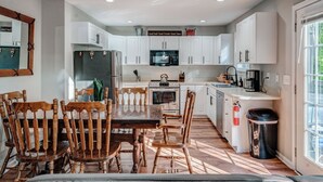 A modern kitchen with white cabinets, a wooden dining table with chairs, a microwave, and a coffee maker. - Cozy Escape • Hot Tub • Overlooks Helen Main Street • Sleeps 9 (Helen)
