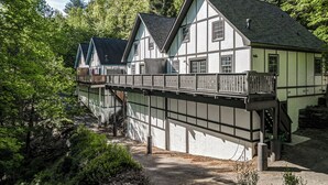 A traditional chalet-style building with a balcony and a wooden deck, surrounded by dense forest. - Cozy Escape • Hot Tub • Overlooks Helen Main Street • Sleeps 9 (Helen)