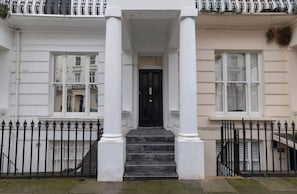 A building with a central entrance flanked by white columns, a black door, and a black metal fence. - Apartment - Sleeps 2 - Paddington Station Close (London)