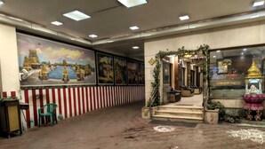 A lobby with a tiled floor, a mural depicting a temple scene, and a reception area with a statue and plants. - Hotel Raya's Annexe 1 (Kumbakonam)
