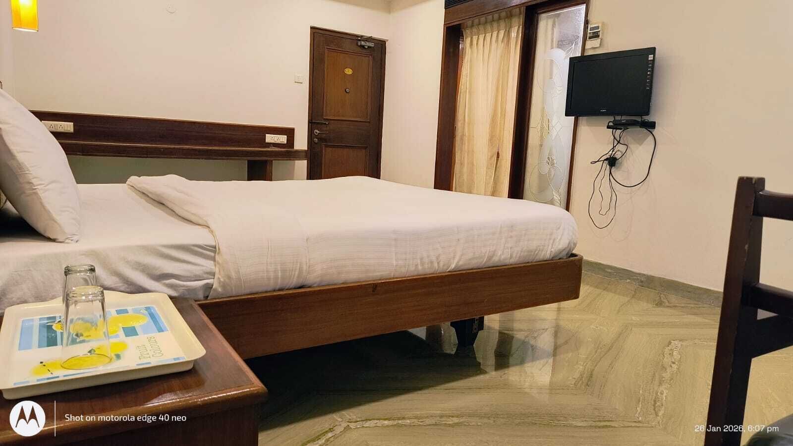A hotel room with a bed, bedside table, and a television mounted on the wall.