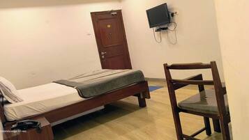 A small, simple room with a single bed, a wooden chair, a television mounted on the wall, and a door.