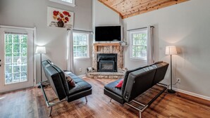 A living room with a stone fireplace, black leather sofas, and a flat-screen TV mounted above it. - Two Homes • Sleeps 18 • Overlooks Downtown Helen • 2 Hot Tubs (Helen)