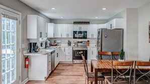 A modern kitchen with white cabinets, a wooden dining table, and a stainless steel refrigerator. - Two Homes • Sleeps 18 • Overlooks Downtown Helen • 2 Hot Tubs (Helen)