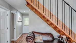 A spacious living room with a leather sofa, a wooden staircase, and a small table with books. - Two Homes • Sleeps 18 • Overlooks Downtown Helen • 2 Hot Tubs (Helen)