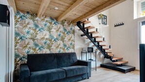 Ein modernes Wohnzimmer mit einem dunkelgrauen Sofa, einer Holztreppe und einer gemusterten Tapete.