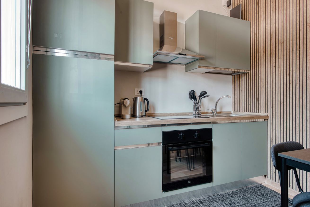 A modern kitchen with a built-in oven, a stainless steel refrigerator, and a wooden wall paneling.