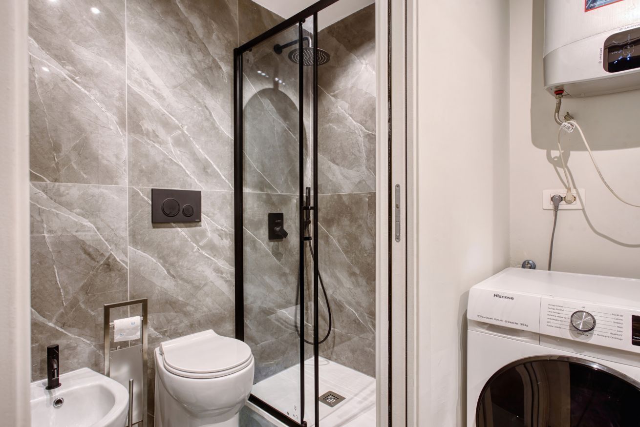 A bathroom with a glass-enclosed shower, a toilet, a sink, and a washing machine.