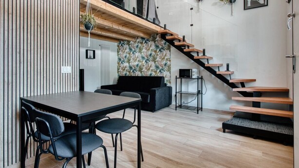 Ein modernes Interieur mit einer Holztreppe, einer Essecke mit Tisch und Stühlen sowie einem schwarzen Sofa.